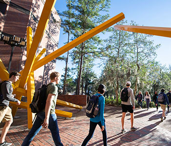 Students walking by yellow sculpture on campus